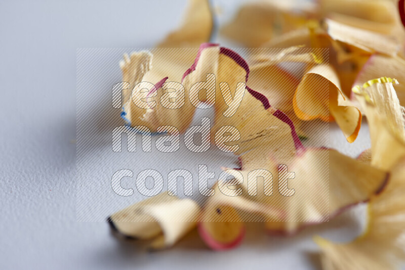 A close-up showing a small pile of pencil shavings with varied color edges on grey background