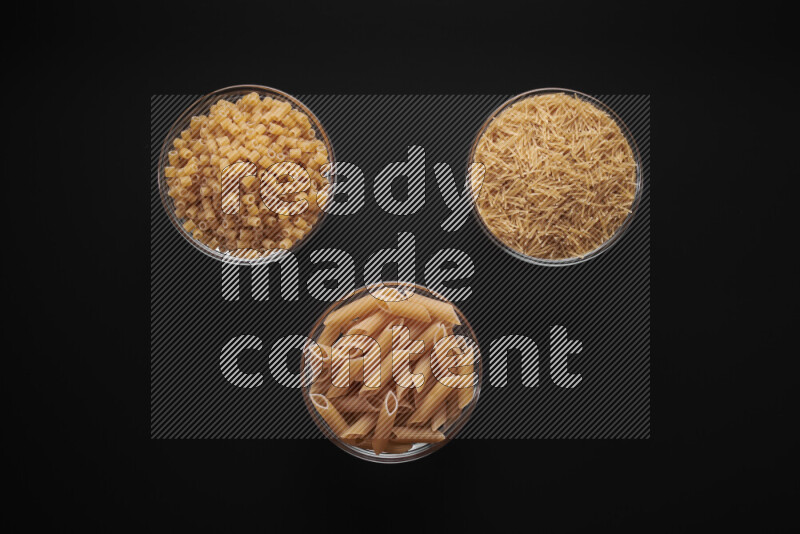 Different pasta types in glass bowls on black background