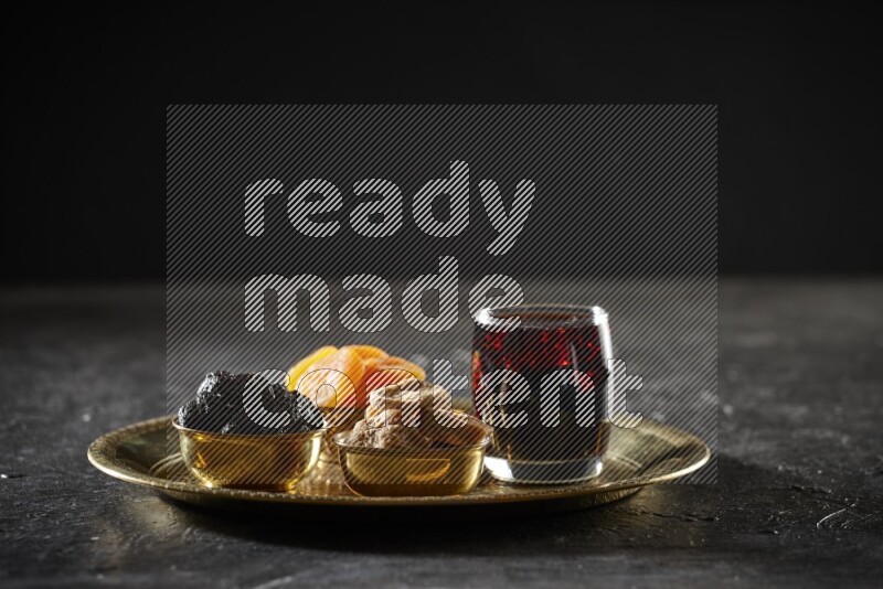 Dried fruits in metal bowls with tamarind on a tray in dark setup
