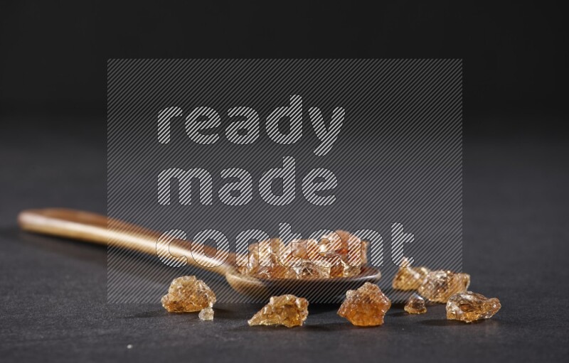 A wooden ladle filled with gum arabic on black flooring