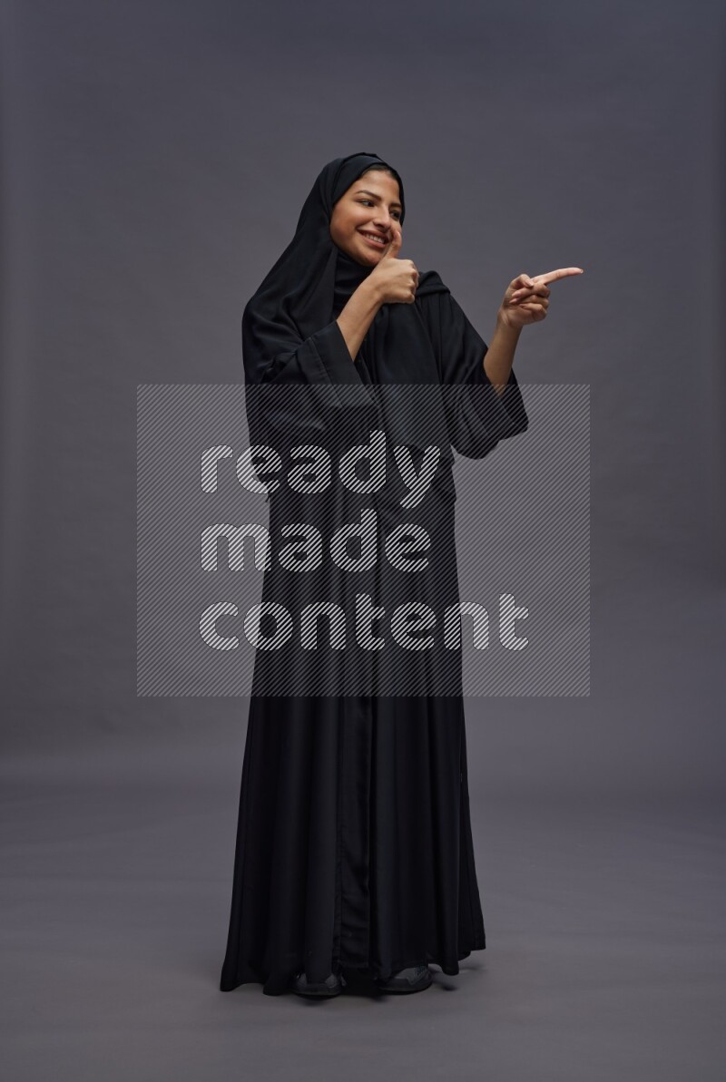 Saudi woman wearing Abaya standing interacting with the camera on gray background