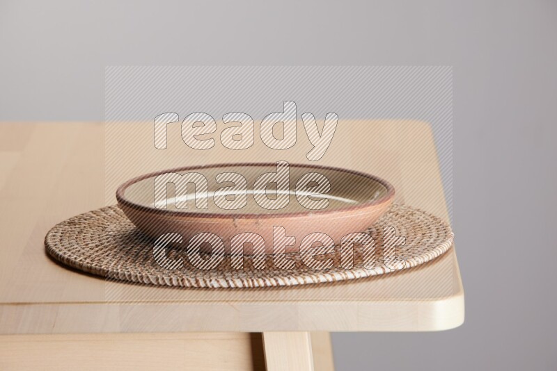 multi-colored pottery Plate placed on a big light colored straw placemat on the edge of wooden table