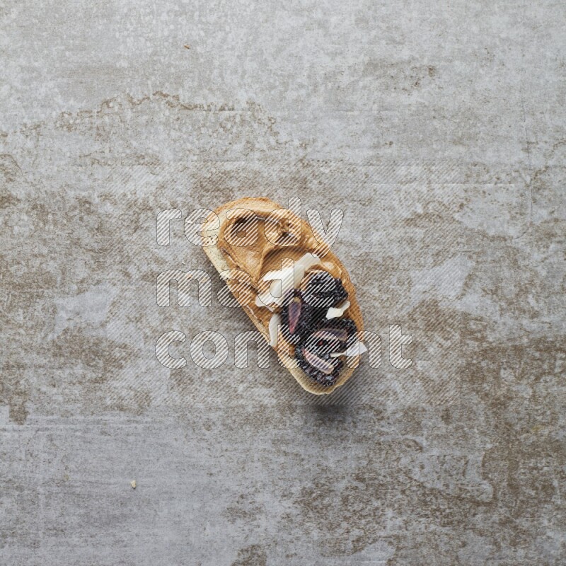open faced peanut butter sandwich with blackberries  and coconut flakes on a  grey textured background