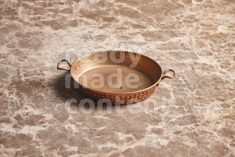 A small copper pan on beige marble background