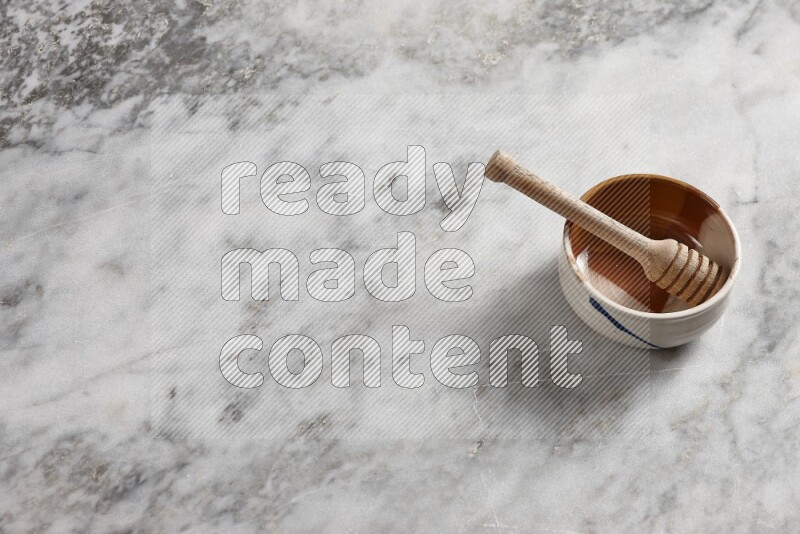 وعاء فخاري متعدد الألوان مع ملعقة عسل خشبية بداخله على خلفية من الرخام الرمادي