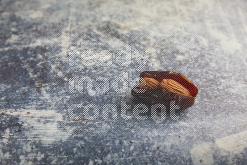 one almond stuffed madjoul dates on a rustic blue background