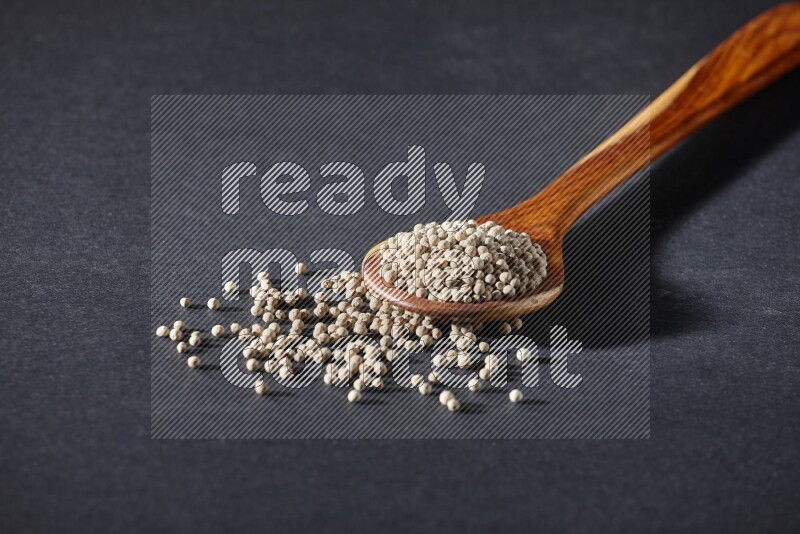 A wooden ladle full of white pepper beads on black flooring