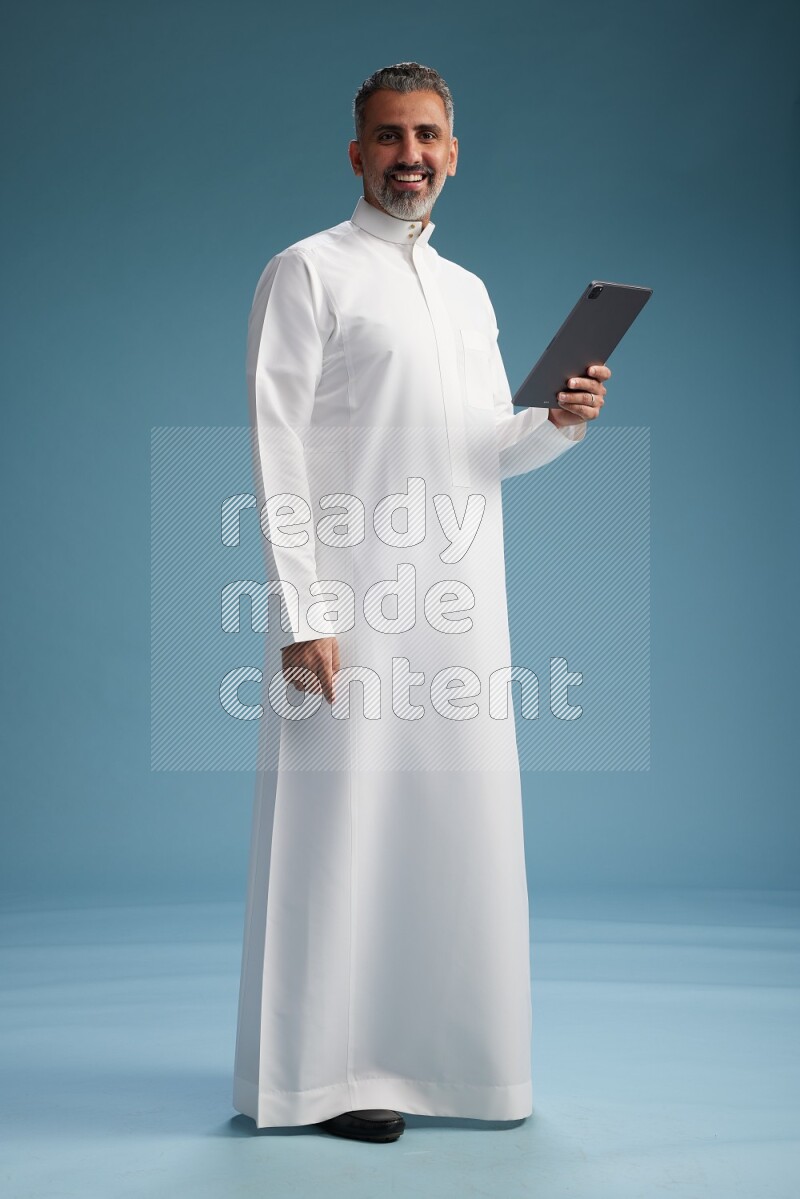 Saudi man waring thob with tablet on blue background