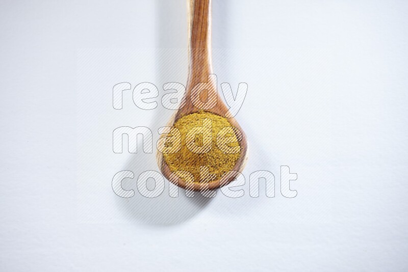 A wooden ladle full of turmeric powder on white flooring