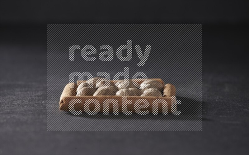 أربعة من أعواد القرفة مكونة شكل مربع بداخلها جوزة الطيب علي خلفية سوداء