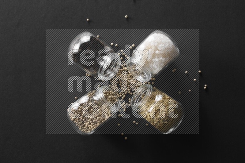 ملح وفلفل أسود وفلفل أبيض وكمون في أوعية زجاجية علي خلفية سوداء