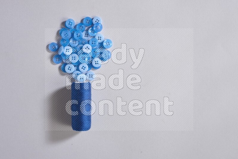 A blue sewing thread spool with colored buttons on grey background