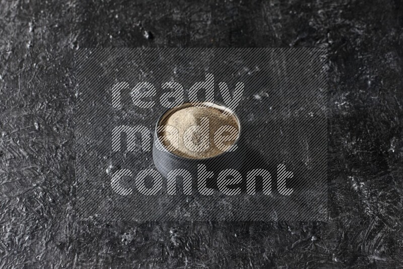 Black pottery bowl full of white pepper powder on textured black flooring