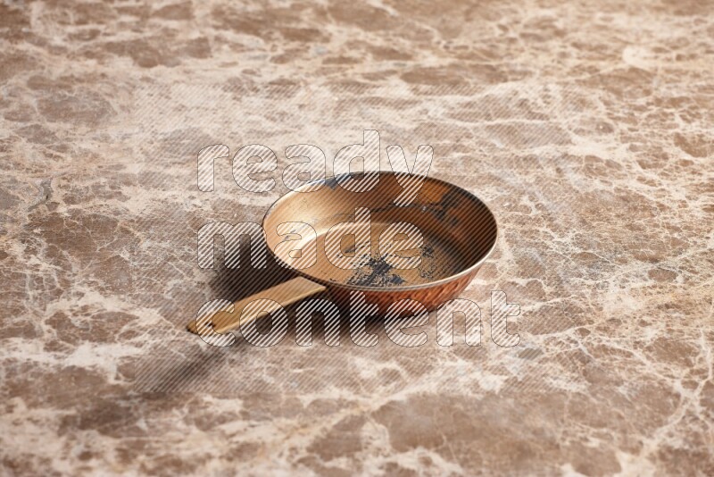 A small copper pan on beige marble background