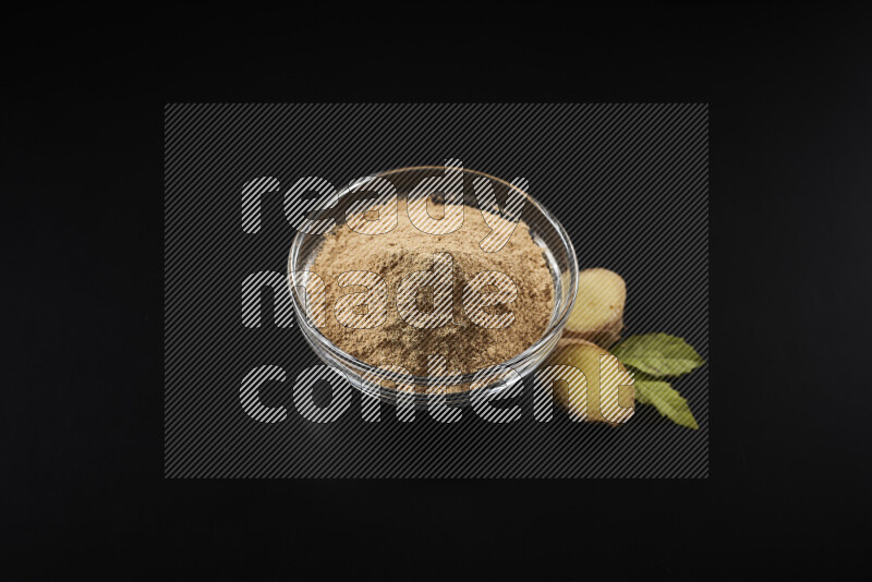 A glass bowl full of ground ginger powder on black background