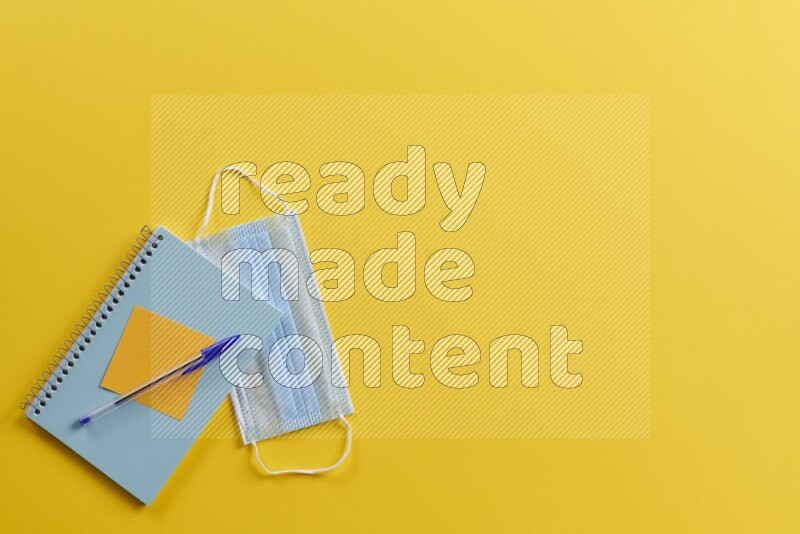 A blue notebook with different school supplies on yellow background