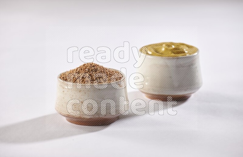 2 beige pottery bowls full of mustard seeds and mustard paste on white flooring in different angles