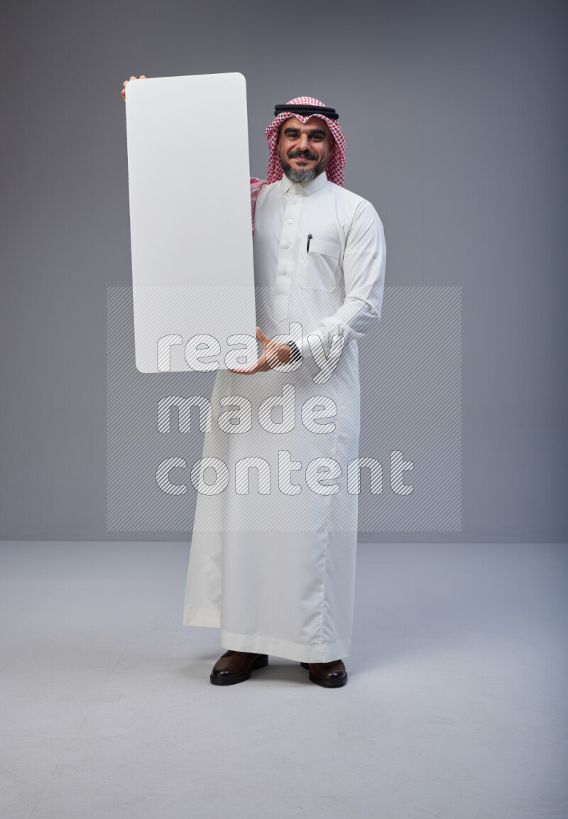 Saudi man Wearing Thob and red Shomag standing holding board on Gray background