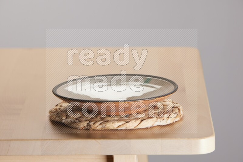 multi-colored pottery Plate placed on a small light colored straw placemat on the edge of wooden table