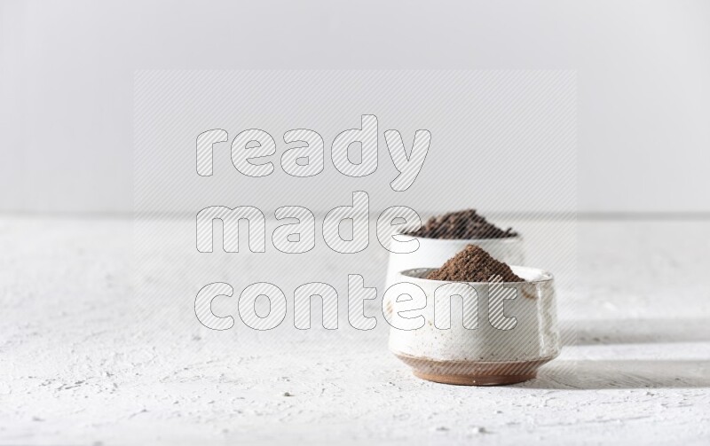 2 Beige ceramic bowls, one full of cloves and the other full of powder on textured white flooring