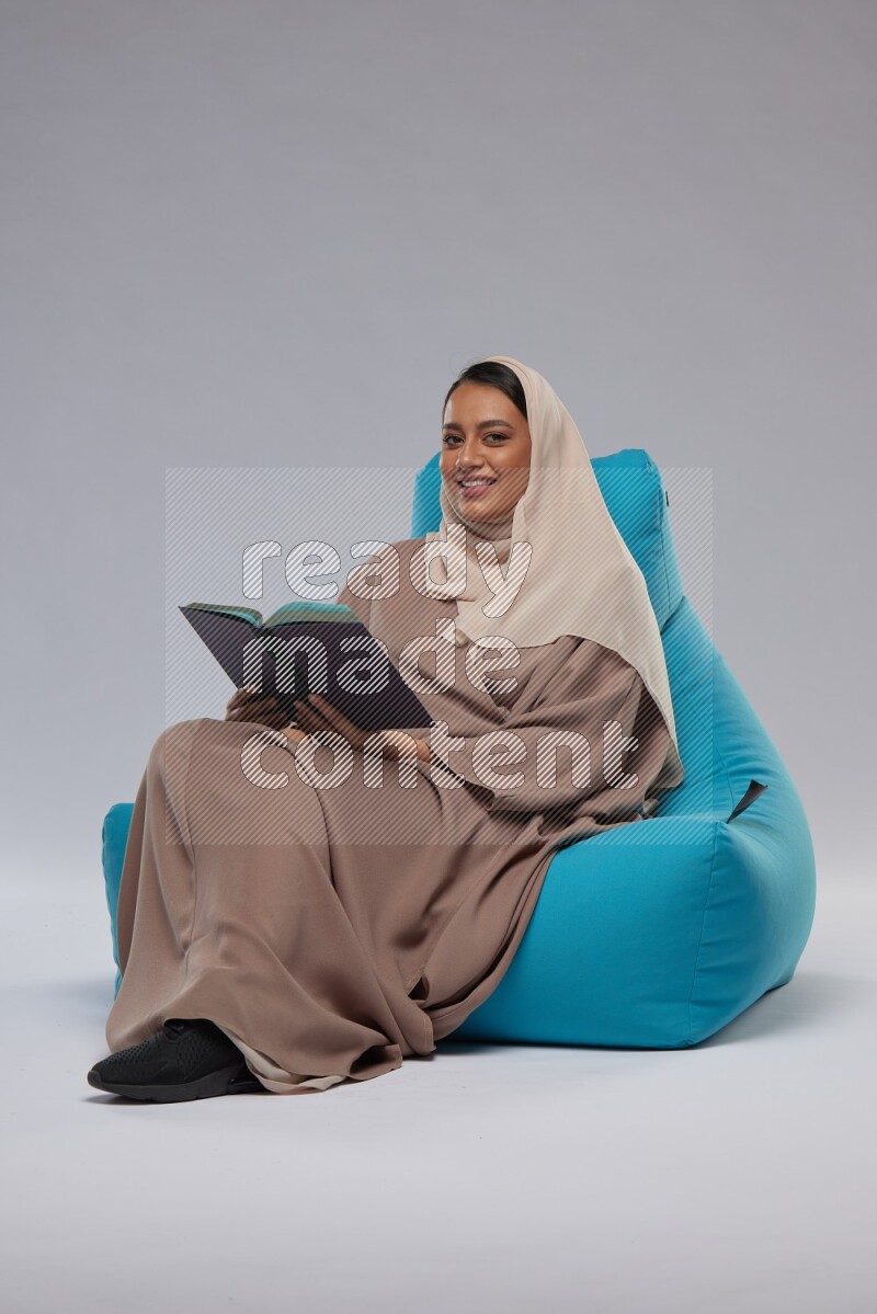 A woman sitting on a blue beanbag and reading a book