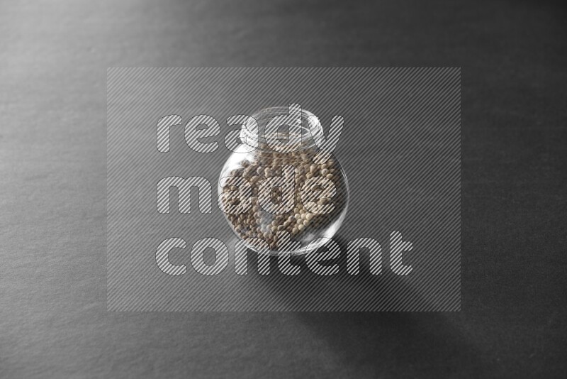 A glass spice jar full of white peppers on black flooring