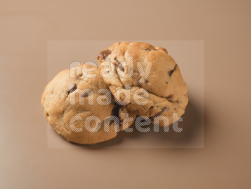 Two chocolate chip cookies on a brown background