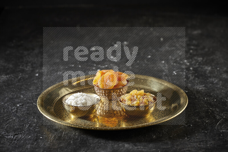 Dried fruits in metal bowls on a tray in a dark setup