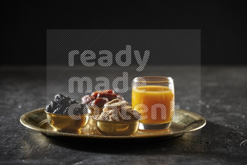 Dried fruits in metal bowls with qamar eldin on a tray in dark setup