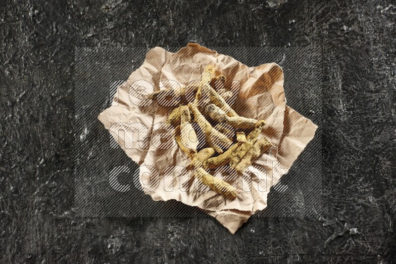 Dried turmeric whole fingers in a crumpled piece of paper on textured black flooring