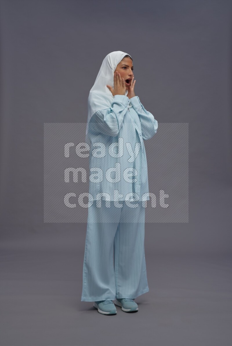 Saudi woman wearing hijab clothes standing interacting with the camera on gray background