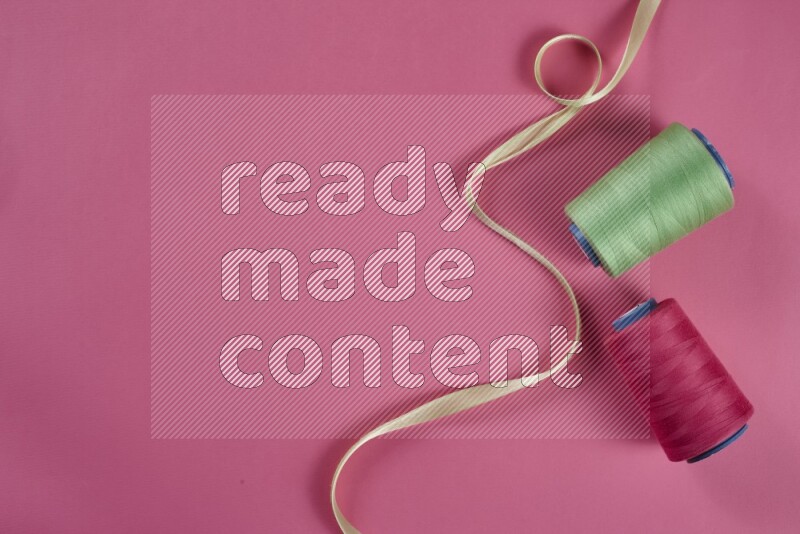 مجموعة من أدوات الخياطة والتفصيل خضراء وزهرية اللون على خلفية زهرية