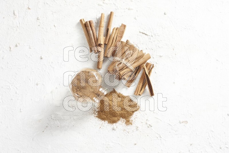 Flipped herbs glass jar full of cinnamon powder and cinnamon sticks in the back on a textured white background