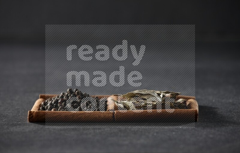 2 squares of cinnamon sticks full of black peppers and bay laurel leaves on black flooring
