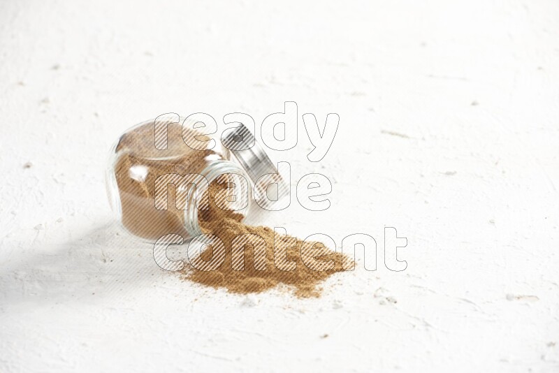 Flipped glass jar full of cinnamon powder on a textured white background