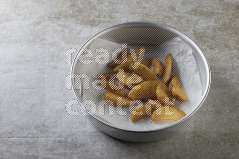 wedges potato on parchment paper in a stainless steel round tray on grey textured counter top