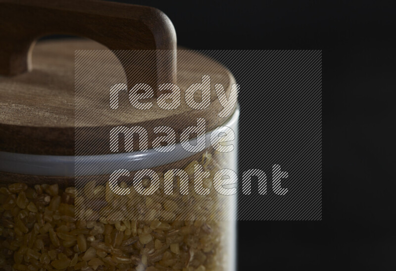 Coarse bulgur in a glass jar on black background