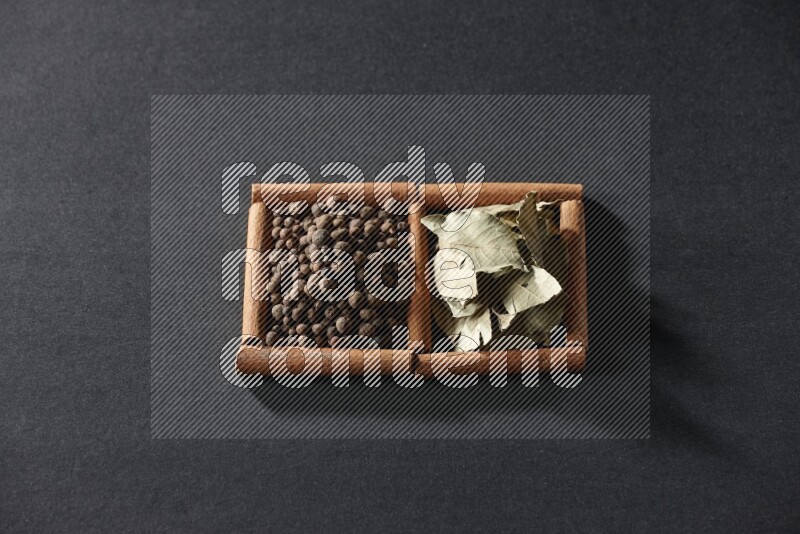 مربعان من أعواد القرفة ممتلئان ببهار الفلفل الحلو وأوراق الغار علي خلفية سوداء