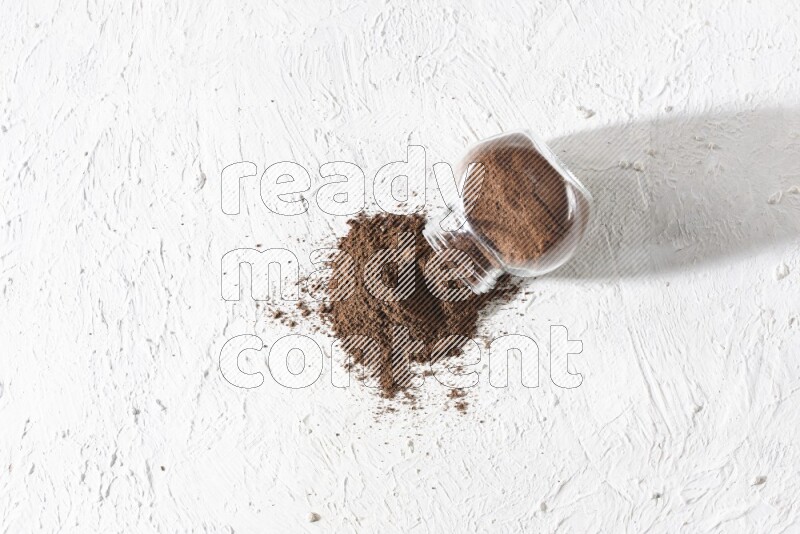 A flipped glass spice jar full of cloves powder and powder came out of it on textured white flooring