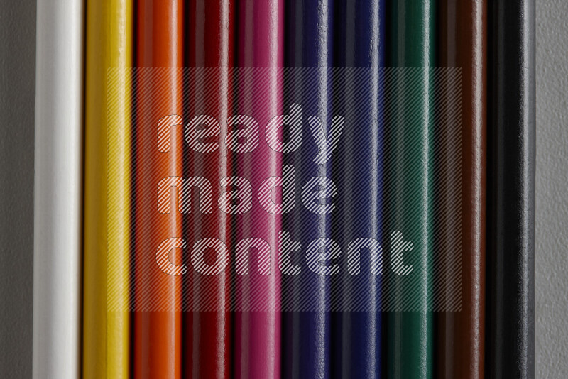 A collection of colored pencils arranged showcasing a gradient of different hues on grey background