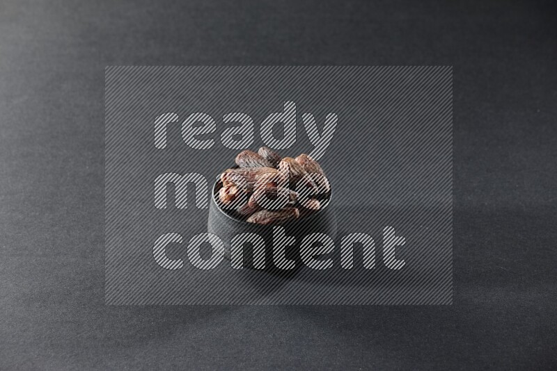A black pottery bowl full of dried dates on a black background in different angles