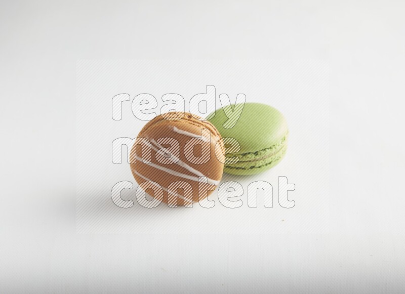 45º Shot of of two assorted Brown Irish Cream, and Green Pistachio macarons on white background