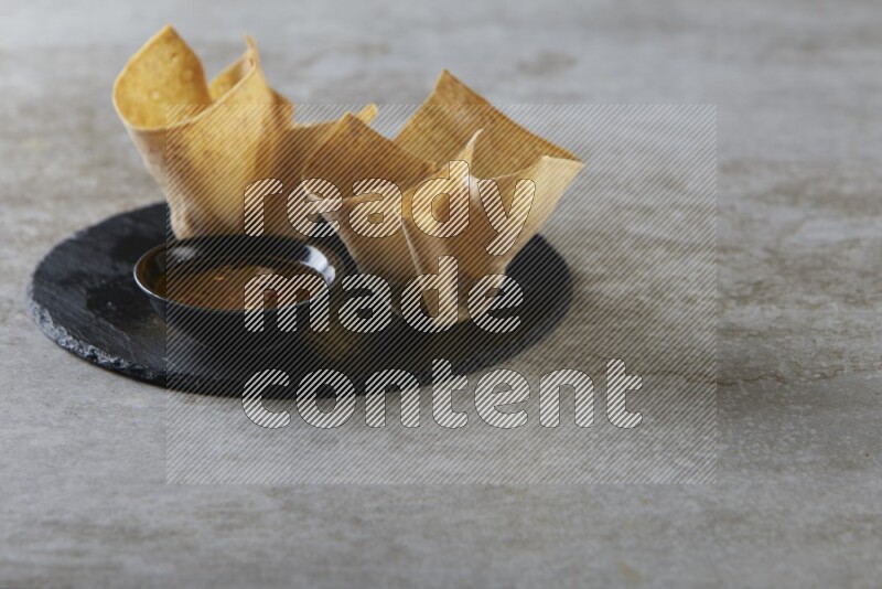 wonton cups with soy sauce ramkin on circle slate on grey textured counter top