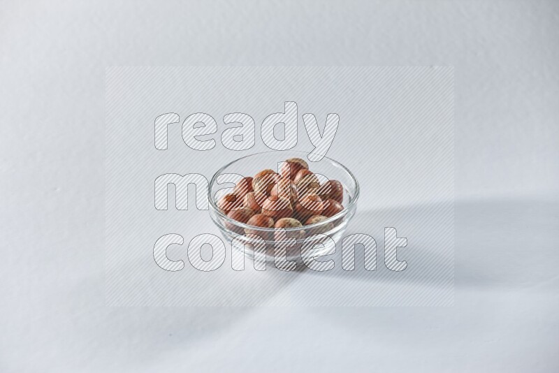 A glass bowl full of hazelnuts on a white background in different angles