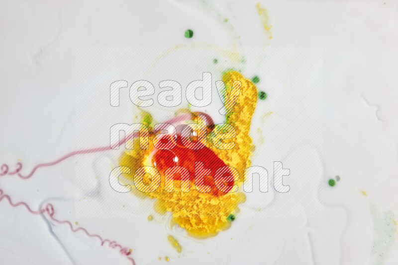 The image captures a splatter of yellow, red and green paint over a white backdrop