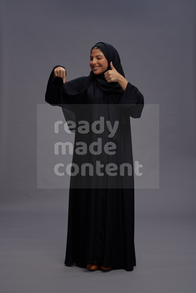 Saudi woman wearing Abaya standing interacting with the camera on gray background