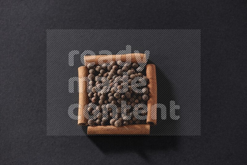 A single square of cinnamon sticks full of allspice on black flooring