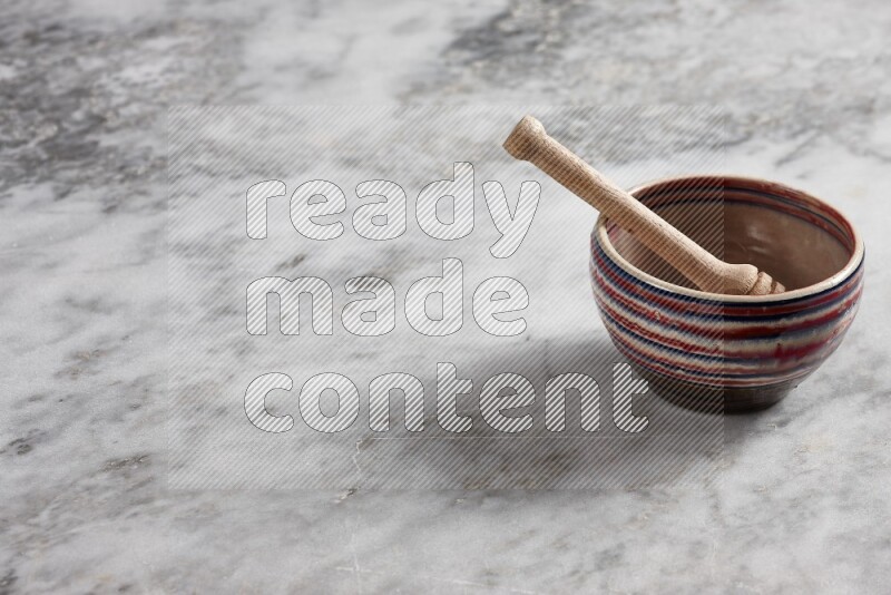 Multicolored pottery bowl with wooden honey dipper in it on grey marble background