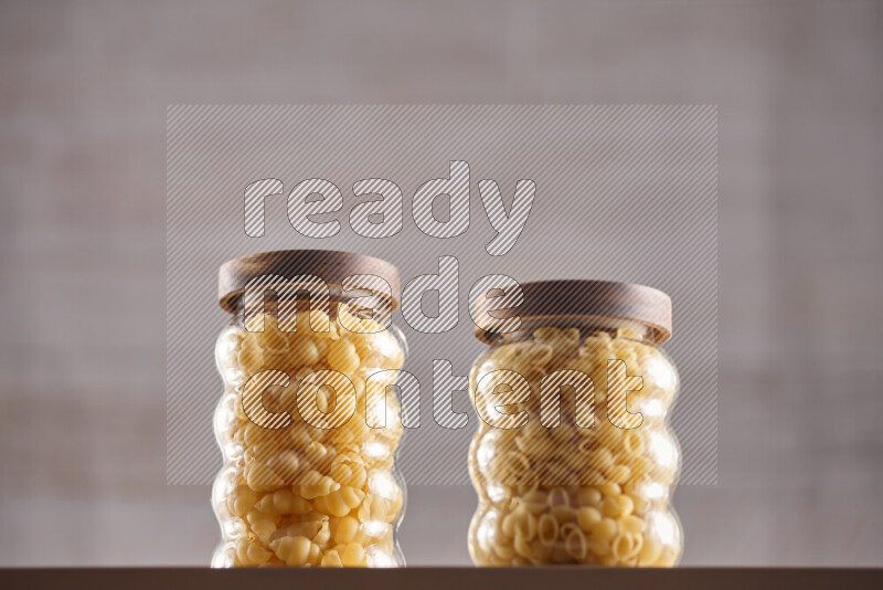 Raw pasta in glass jars on beige background