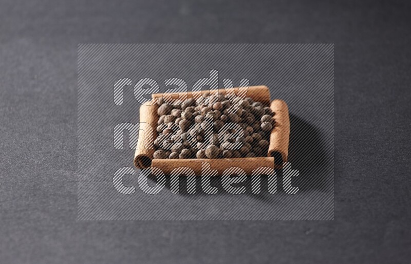 A single square of cinnamon sticks full of allspice on black flooring